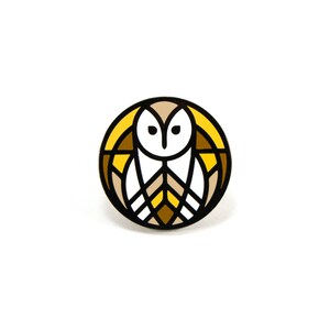 May include: A yellow, brown, and white enamel pin featuring a stylized owl with geometric patterns.