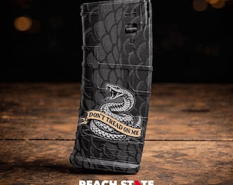 May include: A black magazine with a textured pattern and a graphic of a coiled snake with the text "DON'T TREAD ON ME" on a banner. The magazine is on a wooden surface.
