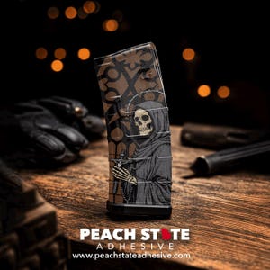 May include: A black and brown magazine with a Grim Reaper design. The image features a skull-faced figure in a hooded robe holding a cross. The magazine has the text "PEACH STATE ADHESIVE" and the website address www.peachstateadhesive.com.