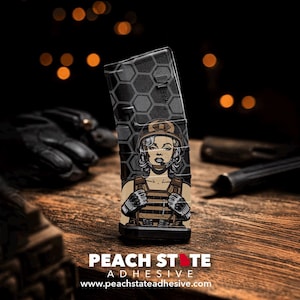 May include: A black magazine with a hexagonal pattern and a graphic of a woman in military gear, reminiscent of Marilyn Monroe. The magazine has the text "PEACH STATE ADHESIVE" and the website address www.peachstateadhesive.com.