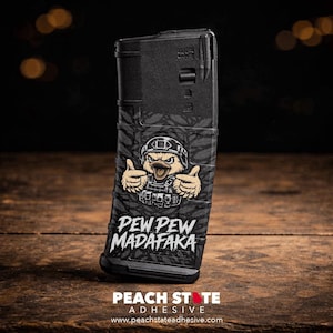 Könnte beinhalten: Schwarzes Magazin mit Tarnmuster und einer Comic-Ente mit Helm und taktischer Weste, die den Daumen hochhält. Der Text "PEW PEW MADAFAKA" ist darunter gedruckt.