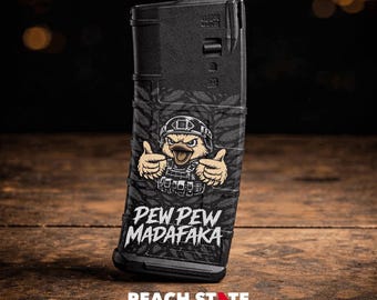 May include: Black magazine with a camouflage pattern and a cartoon duck wearing a helmet and tactical vest, giving a thumbs-up. The text "PEW PEW MADAFAKA" is printed below the duck.