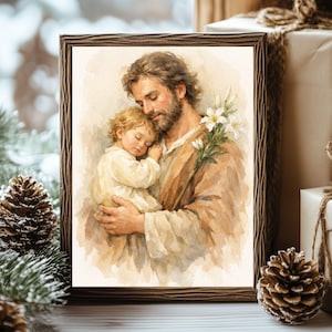Op de afbeelding: Een ingelijste aquarelprint met een bebaarde figuur met bruin haar in een beige gewaad, die een slapend kind in crèmekleurige kleding vasthoudt. De figuur houdt een stengel met witte lelies vast tegen een zachte, neutraal gekleurde achtergrond.
