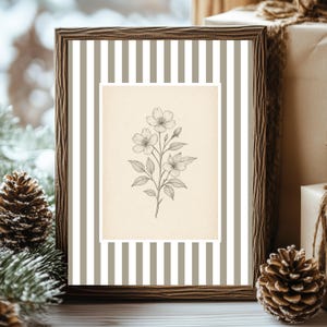 May include: A rectangular picture frame with a dark brown wood-grain texture containing a print. The print features a central cream-coloured rectangle with a detailed black line drawing of a flowering plant with leaves and buds, set against a background of vertical white and beige stripes.