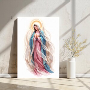 Puede incluir: Impresión en lienzo de una figura religiosa, representada en estilo acuarela. La figura lleva una capa azul sobre un vestido rosa, con un velo blanco y un halo dorado. La obra de arte se exhibe en una pared blanca.