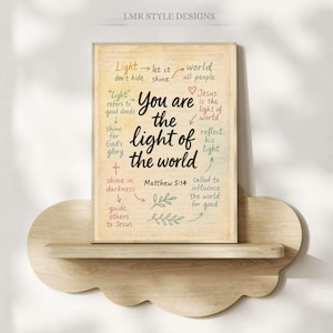 May include: A framed print with the text "You are the light of the world" in a handwritten style. The print is on a wooden shelf shaped like a cloud. The text includes the reference Matthew 5:14.