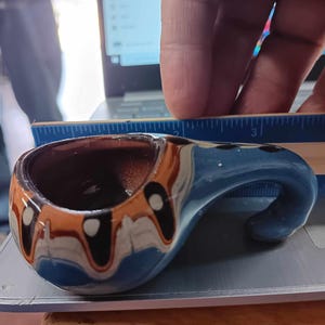 May include: A small, blue, brown, and white ceramic pitcher with a handle. The pitcher has a swirl design and white dots.