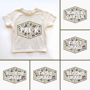 Könnte beinhalten: Beiges kurzärmeliges T-Shirt mit einem sechseckigen Tarnmuster, das den Text "PRE-K" zeigt. Zusätzliche Grafiken zeigen ähnliche Designs für "Kindergarten", "First Grade", "Fourth Grade", "Third Grade" und "Second Grade".