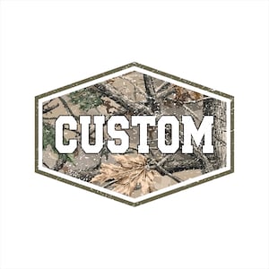 Op de afbeelding: Een aangepast ontwerp met het woord "CUSTOM" in vette, witte blokletters met een zwarte omlijning. De tekst staat tegen een camouflagepatroon in een zeshoekige, olijfgroene lijst. De achtergrond is wit.