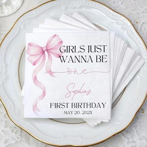 May include: White paper napkins with a pink watercolor bow and the text "GIRLS JUST WANNA BE one Sophia's FIRST BIRTHDAY MAY 20, 202X". Napkins are stacked on a white plate with a gold rim.