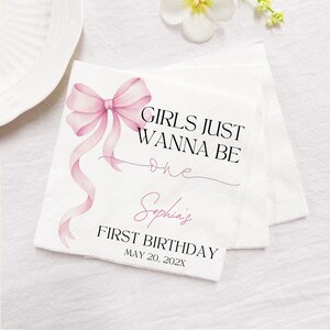 May include: White paper napkins with a pink bow and the text "GIRLS JUST WANNA BE one" and "Sophia's FIRST BIRTHDAY MAY 20, 202X". The napkins are likely for a first birthday celebration.
