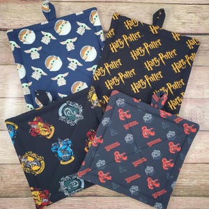 May include: Four square fabric pot holders with hanging loops. One features a blue background with Grogu characters, one is black with yellow Harry Potter text, one is black with colorful Hogwarts house crests, and one is dark gray with red Dungeons and Dragons logos.