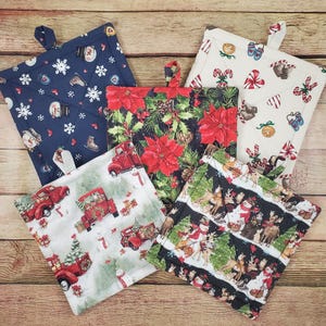 May include: Five square quilted pot holders featuring various holiday patterns including red trucks with Christmas trees, poinsettias, snowmen, snowflakes, candy canes, and woodland animals. Each fabric square has a small hanging loop at the top.