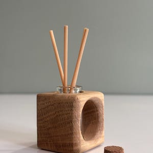 May include: A wooden diffuser stand with a round opening for a glass bottle and diffuser sticks. The stand is made of light brown wood and has a cork stopper.