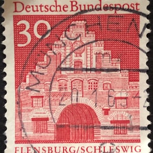 Puede incluir: Un sello postal alemán rojo y blanco con una imagen de un edificio y el texto "Deutsche Bundespost" y "30" en la esquina superior izquierda. El texto "Flensburg/Schleswig" está en la parte inferior del sello.
