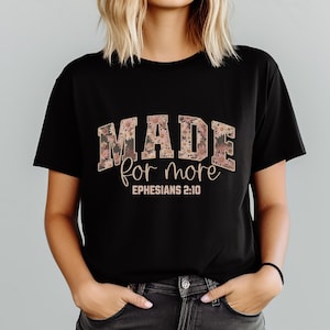 May include: Black t-shirt with the words "MADE for more" in a floral design. The text "Ephesians 2:10" is below the main text. The shirt is short-sleeved and has a crew neck.