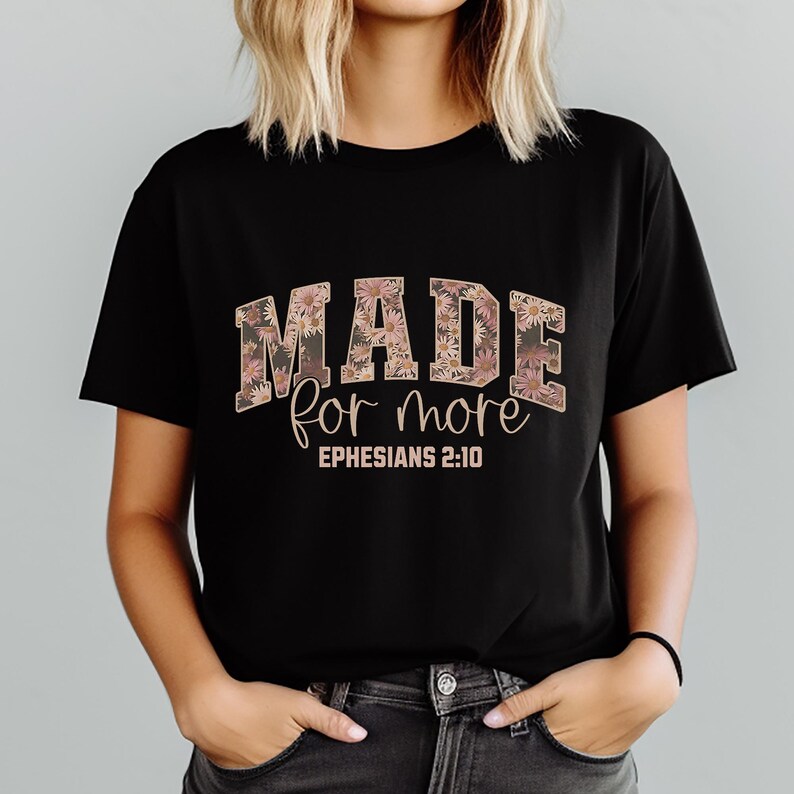 May include: Black t-shirt with the words "MADE for more" in a floral design. The text "Ephesians 2:10" is below the main text. The shirt is short-sleeved and has a crew neck.