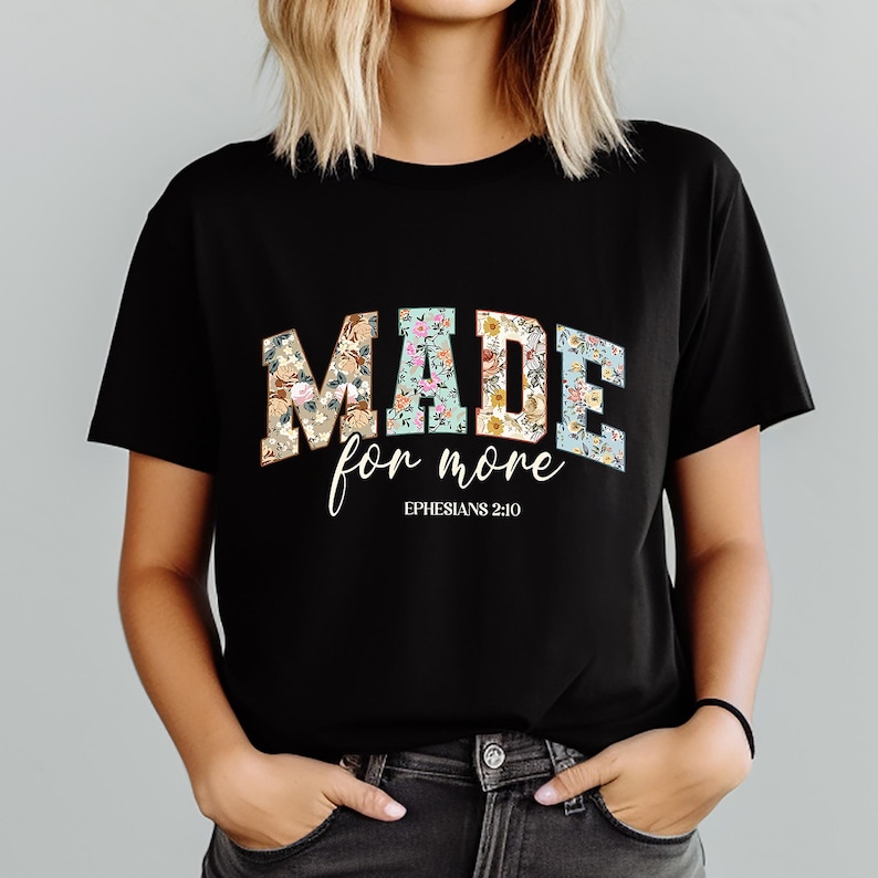 May include: Black t-shirt with the words "MADE for more" in a floral design. The text "Ephesians 2:10" is below the main text in a script font. The shirt is a crew neck style.