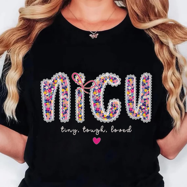 May include: Black t-shirt with the letters "NICU" in a floral design, outlined with white lace. A pink bow is between the "N" and "C". Below the letters, the words "tiny, tough, loved" are written, with a pink heart below.