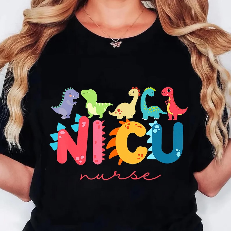 May include: Black t-shirt featuring colorful dinosaurs above the text "NICU nurse" in a playful font. The dinosaurs are in various colors, including purple, green, yellow, and red. The shirt is a casual style.