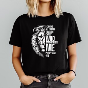 Może przedstawiać: Czarny t-shirt z białym motywem głowy lwa i napisem "I CAN DO ALL THINGS THROUGH CHRIST WHO STRENGTHENS ME PHILIPPIANS 4:13". Grafika to szczeg&oacute;łowa ilustracja głowy lwa z koroną.