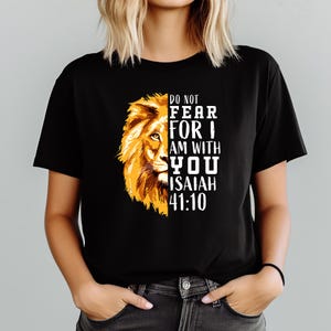 Może przedstawiać: Czarny t-shirt z złotą grafiką lwa po lewej stronie i białym tekstem "DO NOT FEAR FOR I AM WITH YOU ISAIAH 41:10". Koszulka ma kr&oacute;tkie rękawy i okrągły dekolt.