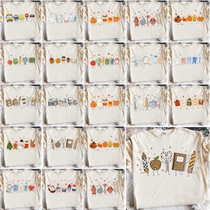 Puede incluir: Una colección de camisetas de color blanco roto, cada una con una fila de ilustraciones coloridas de estilo caricatura de varios objetos con caras sonrientes, incluyendo útiles escolares, temas festivos, herramientas médicas y alimentos.