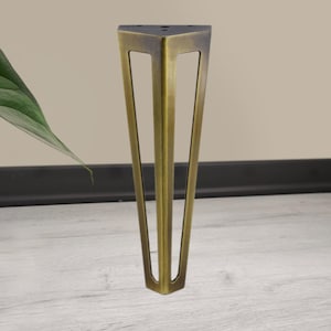 May include: A single, bronze-colored furniture leg with a triangular design. The leg has a flat top with three screw holes and tapers down to a pointed base. The leg is made of metal and has a vintage or antique appearance.