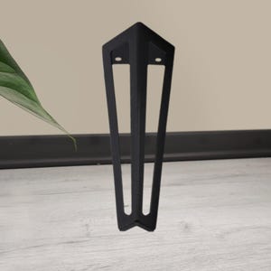 May include: A black metal furniture leg with a geometric design. The leg has a triangular top with two holes and three vertical supports that taper to a point. The leg is designed to be mounted on a piece of furniture.