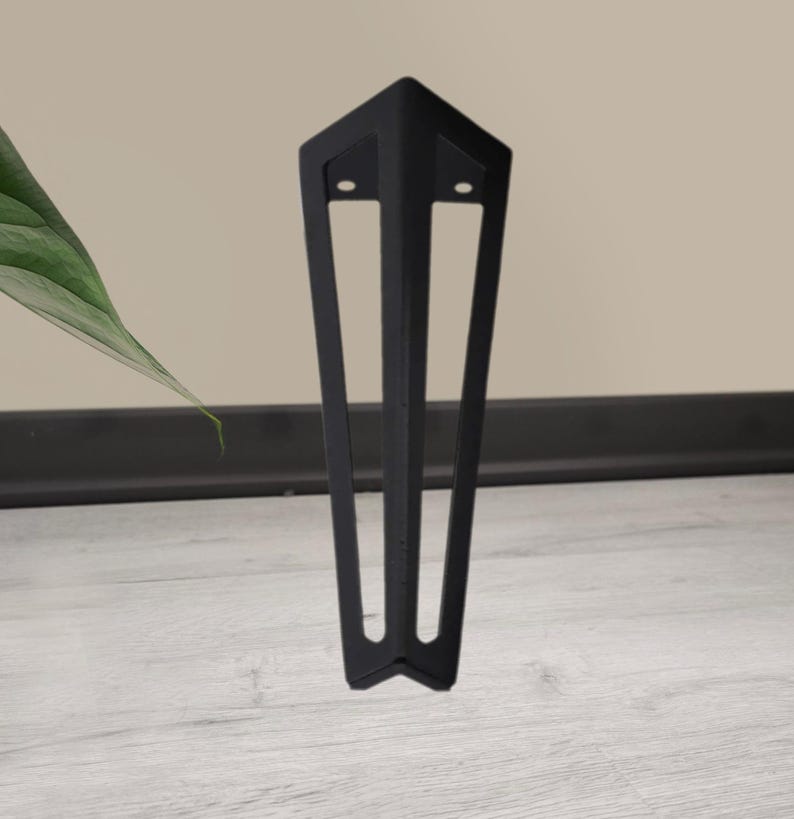 May include: A black metal furniture leg with a geometric design. The leg has a triangular top with two holes and three vertical supports that taper to a point. The leg is designed to be mounted on a piece of furniture.