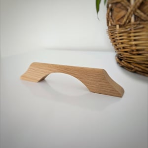 Op de afbeelding: Een lichtbruine houten kastknop met een gebogen boog.