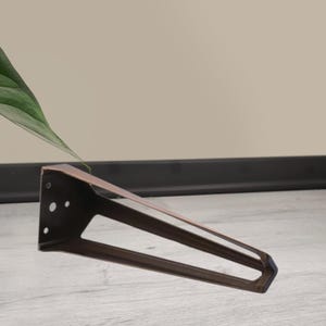 May include: A bronze-colored, angled metal furniture leg with a triangular design. The leg has a flat top with pre-drilled holes for mounting and a tapered, open-frame base. The leg is designed for furniture construction and repair.