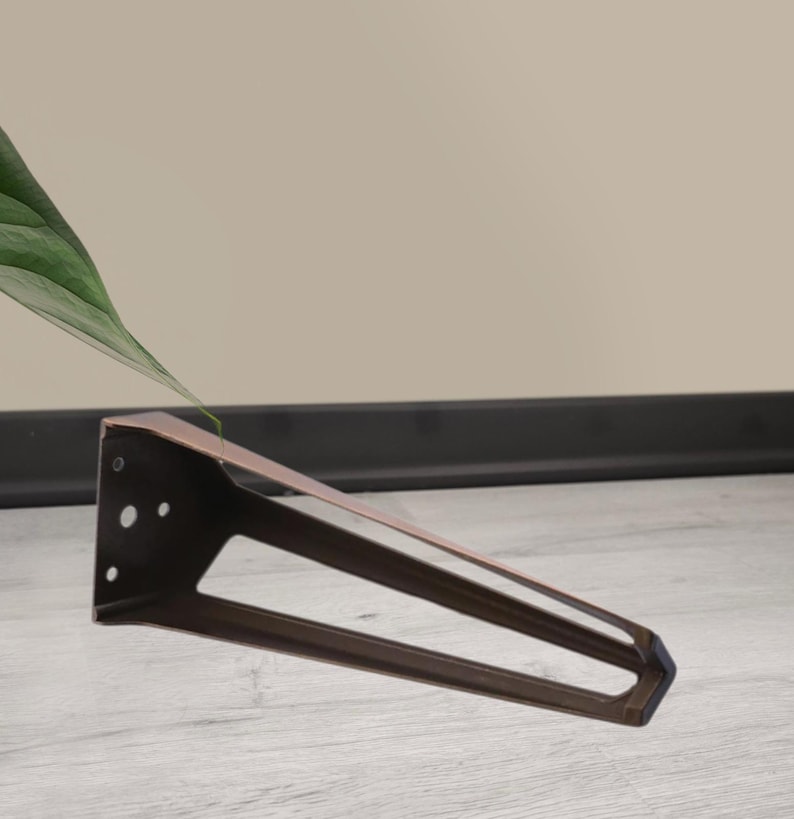 May include: A bronze-colored, angled metal furniture leg with a triangular design. The leg has a flat top with pre-drilled holes for mounting and a tapered, open-frame base. The leg is designed for furniture construction and repair.