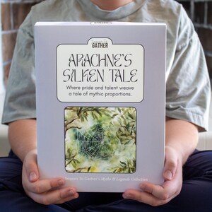 以下が含まれることがあります： 「Arachne's Silken Tale」というタイトルの白い箱と、森の中のクモの巣の水彩画が描かれています。テキストには「Where pride and talent weave a tale of mythic proportions.」と書かれています。この箱は「Season To Gather's Myths & Legends Collection.」の一部です。