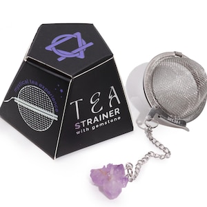 May include: A silver tea strainer with a chain and a purple amethyst gemstone. The strainer is in a black box with the text "TEA STRAINER with gemstone" and "mystical tea experience".