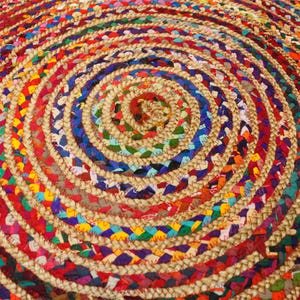May include: A round, multi-colored braided rug with a circular pattern. The rug is made of natural fibers and features a variety of colors, including red, blue, green, yellow, and brown.