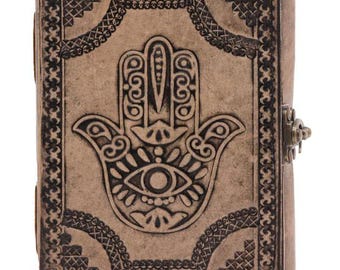 May include: A brown leather journal with a hamsa hand design embossed on the front cover. The journal has a decorative border and a brass clasp.