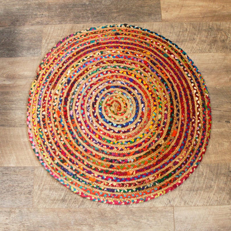 May include: A round, multi-colored jute rug with a circular pattern. The rug is made of braided strands of jute in shades of red, orange, yellow, green, blue, purple, and brown.