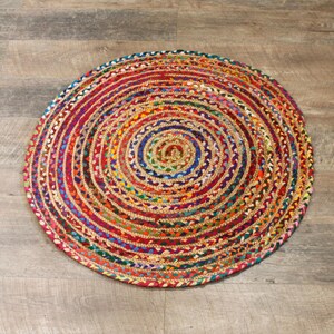 May include: A round, multi-colored jute rug with a braided design. The rug has a variety of colors, including red, blue, green, yellow, and orange.