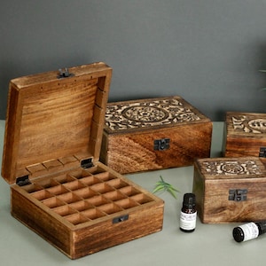 May include: Wooden essential oil storage boxes with carved floral patterns. One box is open, showing multiple compartments. The boxes are various sizes and have metal clasps. A small bottle of essential oil is visible.