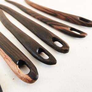 May include: Five wooden knitting needles with a dark brown stain and a natural wood color at the tip. The needles have a small loop at the end.