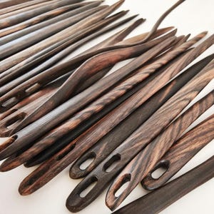 May include: A set of wooden knitting needles with dark brown and black wood grain. The needles have a smooth, polished finish and are designed for knitting projects.