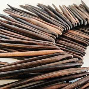 May include: A close-up of a wall art piece made of dark brown wooden sticks arranged in a fan shape. The sticks are all different lengths and have a natural, rustic look.