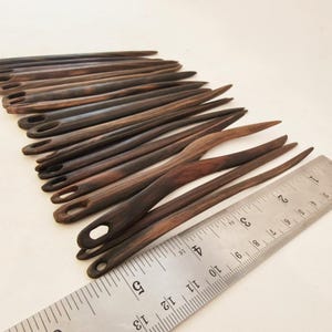 May include: A set of 18 wooden knitting needles with a dark brown finish. The needles are approximately 5 inches long and have a rounded tip. The needles are arranged in a fan shape and are measured against a ruler.