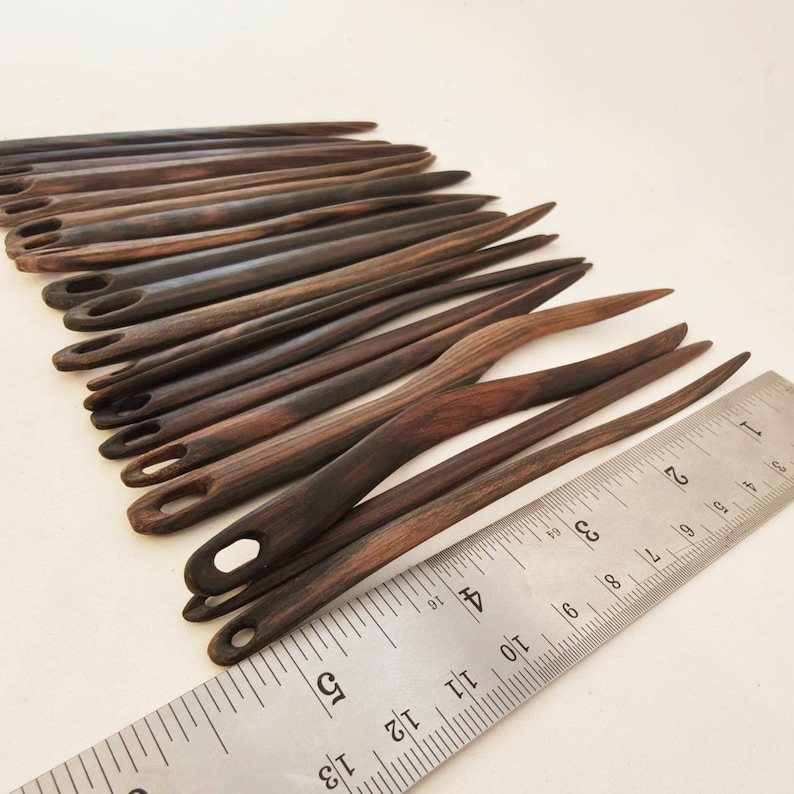 May include: A set of 18 wooden knitting needles with a dark brown finish. The needles are approximately 5 inches long and have a rounded tip. The needles are arranged in a fan shape and are measured against a ruler.