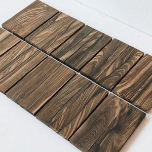 May include: A collection of rectangular wooden blocks with a dark brown and black grain pattern. The blocks are arranged in rows, showcasing the natural wood grain. The wood has a rich, textured appearance, suitable for crafting or decorative projects.