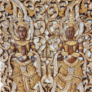 May include: A pair of rectangular wooden wall panels featuring intricate hand-carved figures in a prayer pose. The dark brown wood is adorned with gold-painted accents and numerous small, reflective circular mirror inlays throughout the design.