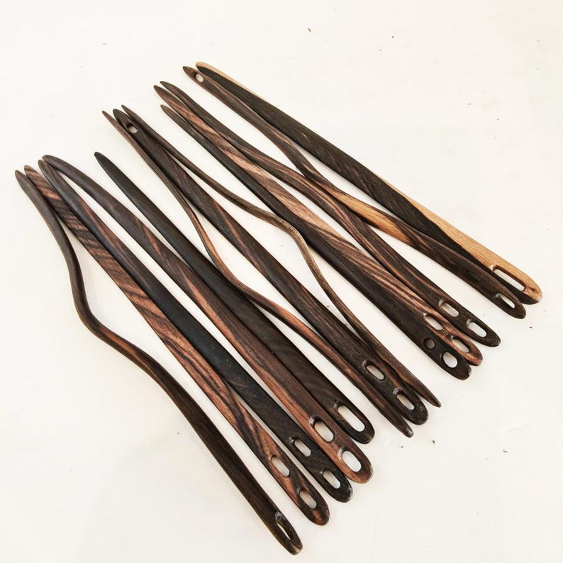 May include: A set of 15 wooden knitting needles with a dark brown and light brown wood grain pattern. The needles have a rounded tip and a hole at the end for threading yarn.