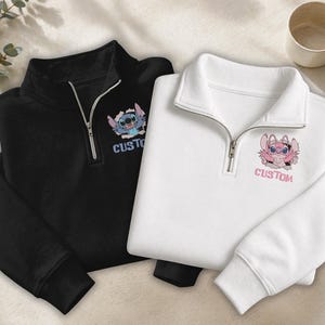 May include: Two pullover sweatshirts, one black and one white, with a quarter-zip collar. Each sweatshirt features a cartoon character graphic and the word "CUSTOM" printed below. The black sweatshirt has a blue and white character, while the white one has a pink character.