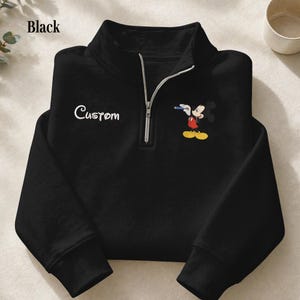 Puede incluir: Sudadera negra con cremallera de cuarto de cuello con texto "Custom" blanco y un gr&aacute;fico de Mickey Mouse. El personaje de dibujos animados es rojo, amarillo y negro. La sudadera tiene una cremallera plateada y un cuello alto.